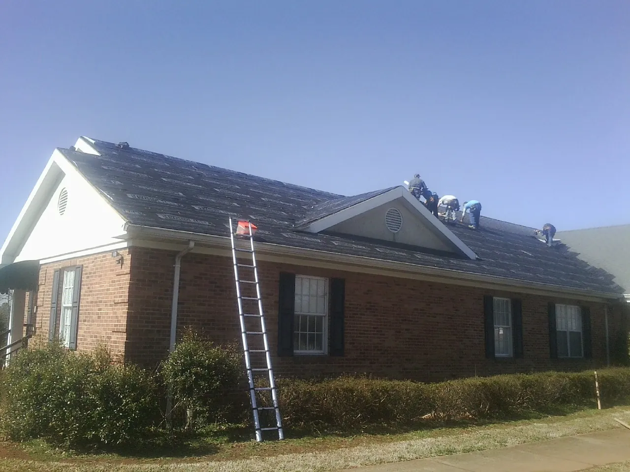 Crew tearing shingles off a brick ranch roof with a ladder set — Metal Roof Repair work by our crew in Cos Cob
