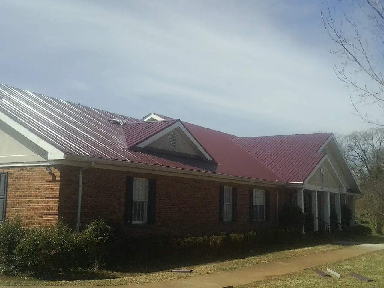 Red metal roof with gabled entries on a long brick building, from a Hail Damage Roof Repair job in Cos Cob