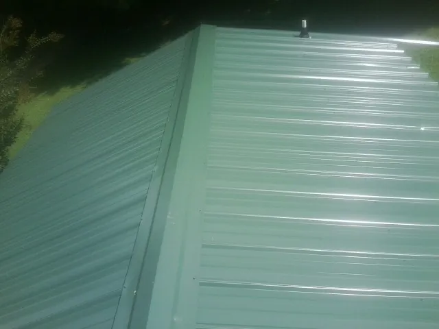 New green metal panels meeting at the ridge of a roof — Flat Roof Repair work by our crew in Cos Cob